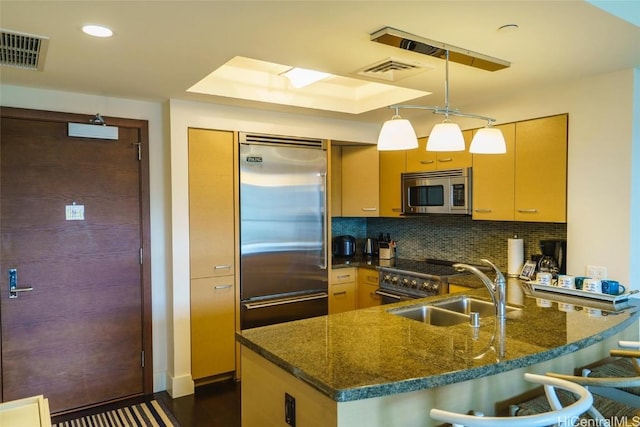 kitchen featuring sink, dark stone countertops, backsplash, high quality appliances, and decorative light fixtures