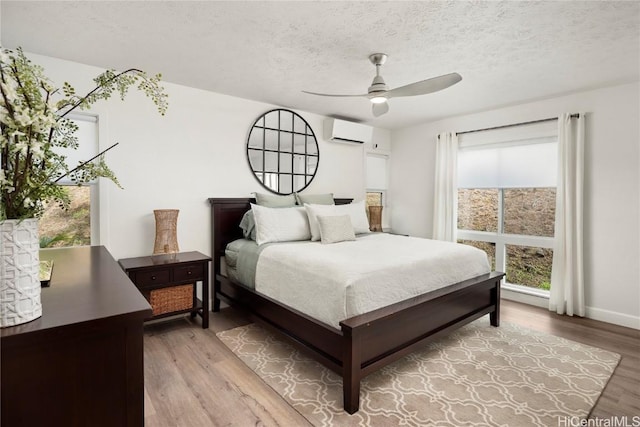 bedroom featuring hardwood / wood-style flooring, ceiling fan, a wall unit AC, and a textured ceiling