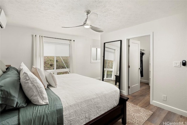 bedroom with ceiling fan, hardwood / wood-style floors, a textured ceiling, and an AC wall unit