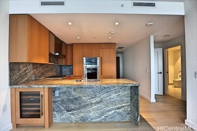 kitchen with double oven, tasteful backsplash, wine cooler, black electric stovetop, and light hardwood / wood-style floors