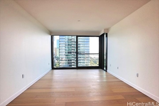 empty room with expansive windows, a healthy amount of sunlight, and light hardwood / wood-style flooring