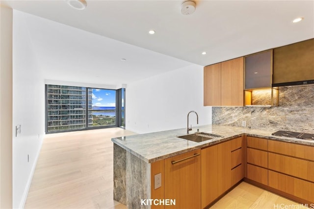 kitchen with light stone counters, stainless steel gas stovetop, backsplash, a sink, and a peninsula