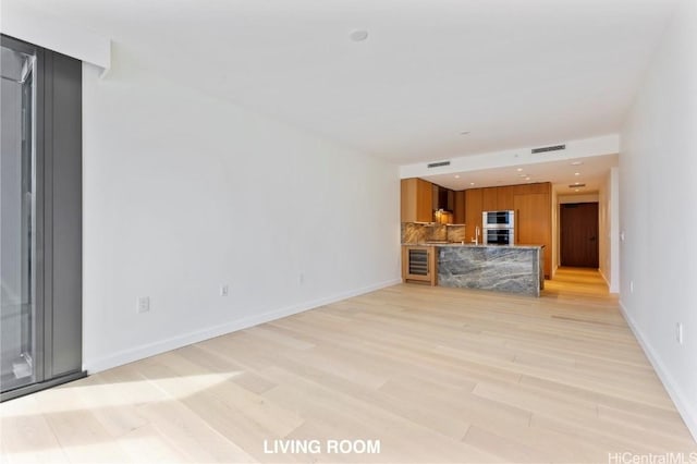 unfurnished living room with light wood-type flooring, beverage cooler, visible vents, and baseboards