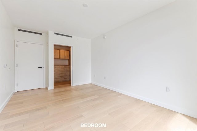 unfurnished bedroom featuring light wood-style floors, visible vents, a spacious closet, and baseboards