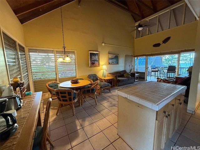 kitchen featuring light tile patterned floors, ceiling fan, tile counters, decorative light fixtures, and beamed ceiling