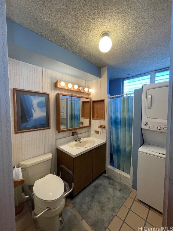 bathroom with tile patterned flooring, vanity, stacked washer / drying machine, a textured ceiling, and walk in shower