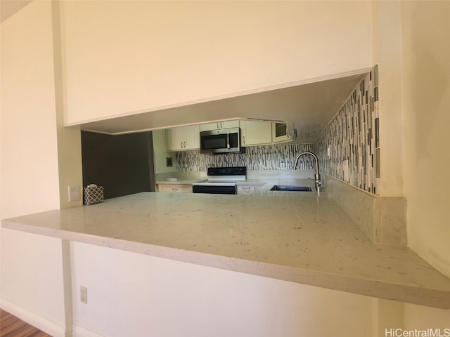 kitchen featuring stainless steel microwave, light stone countertops, electric range oven, a peninsula, and a sink