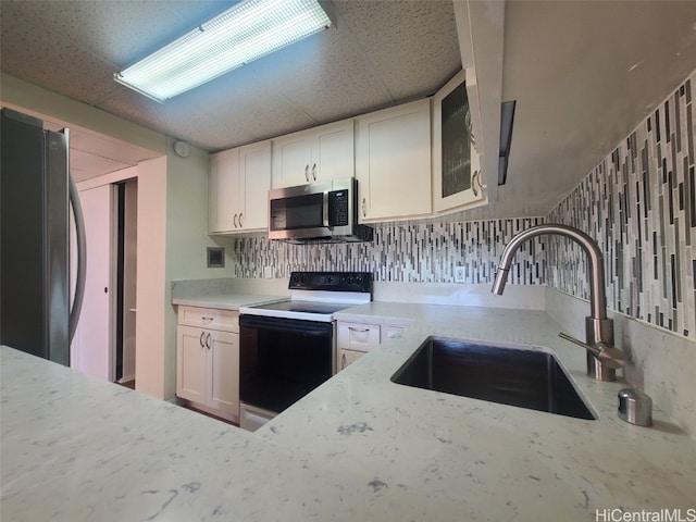 kitchen featuring stainless steel microwave, light stone countertops, electric range oven, freestanding refrigerator, and a sink