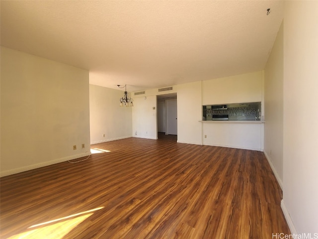 unfurnished living room featuring visible vents, baseboards, a notable chandelier, and dark wood-style flooring