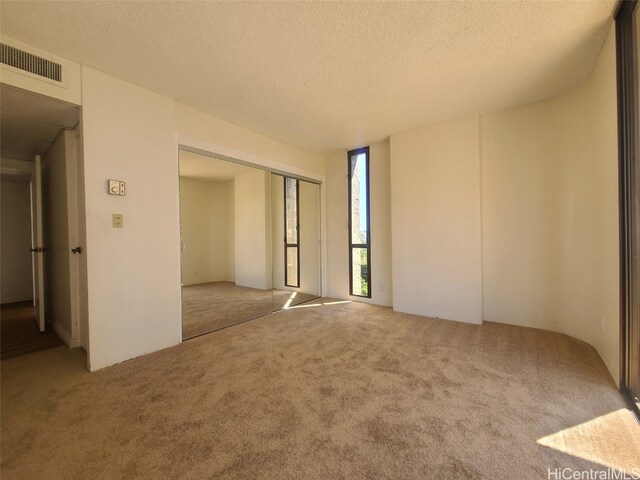 unfurnished room featuring visible vents, a textured ceiling, and carpet flooring