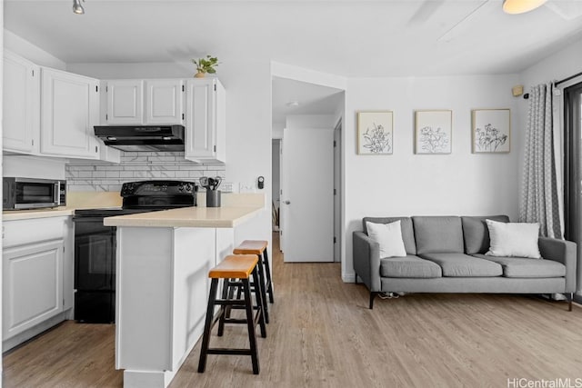 kitchen featuring white cabinetry, black electric range oven, a breakfast bar area, and decorative backsplash