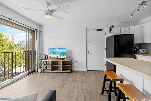 kitchen featuring light hardwood / wood-style flooring, ceiling fan, a kitchen bar, white cabinets, and black fridge