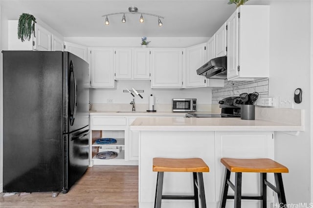 kitchen with black refrigerator, white cabinetry, kitchen peninsula, and exhaust hood