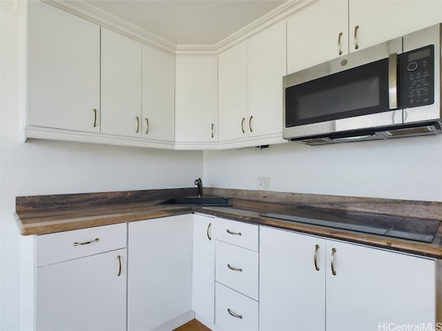 kitchen with ornamental molding, black electric stovetop, and white cabinets