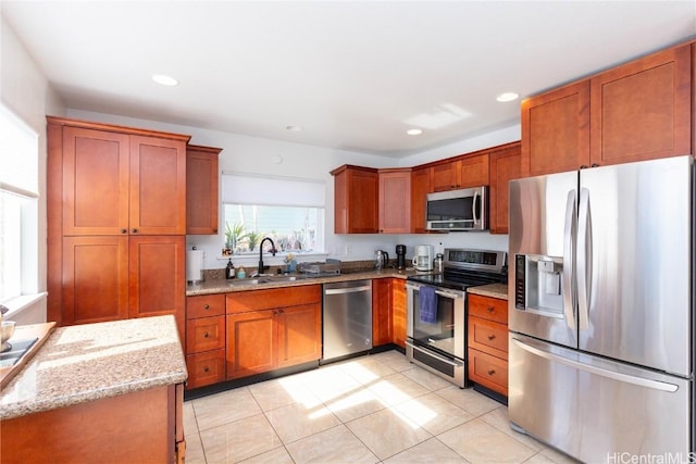 kitchen with light stone countertops, appliances with stainless steel finishes, sink, and light tile patterned flooring