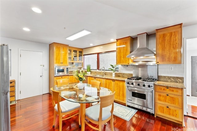 kitchen featuring appliances with stainless steel finishes, sink, dark hardwood / wood-style flooring, light stone countertops, and wall chimney exhaust hood