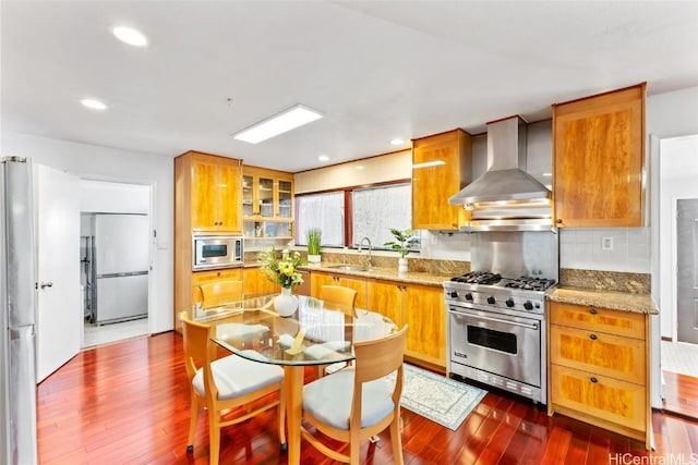 kitchen featuring sink, dark hardwood / wood-style floors, built in appliances, light stone countertops, and wall chimney exhaust hood