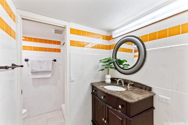 bathroom with toilet, tile walls, a textured ceiling, vanity, and tile patterned flooring