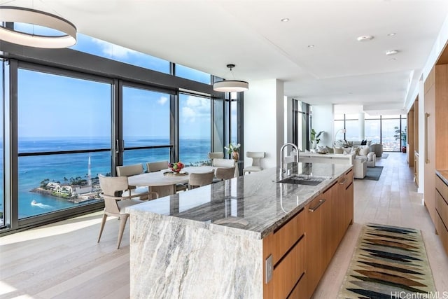 kitchen with sink, stone counters, a water view, expansive windows, and an island with sink