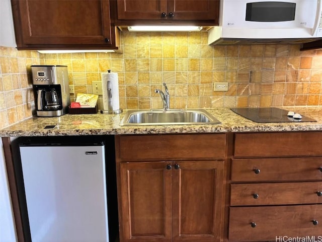 kitchen with tasteful backsplash, stainless steel fridge, light stone countertops, and sink