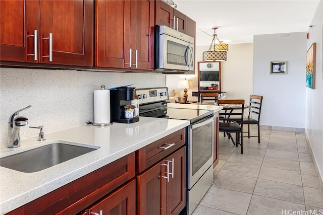 kitchen with light stone counters, appliances with stainless steel finishes, decorative light fixtures, and sink