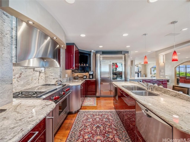 kitchen featuring pendant lighting, sink, high end appliances, ventilation hood, and light stone countertops