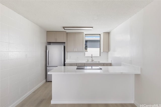 kitchen with stainless steel refrigerator, sink, light hardwood / wood-style floors, kitchen peninsula, and a textured ceiling