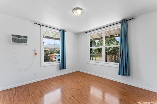 spare room with a wall mounted air conditioner, wood finished floors, and baseboards