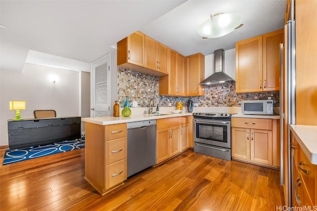 kitchen featuring sink, light wood-type flooring, appliances with stainless steel finishes, wall chimney range hood, and backsplash