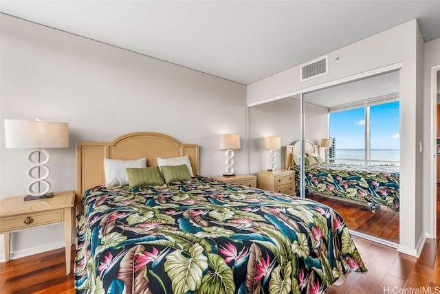 bedroom with dark wood-type flooring, a water view, and a closet