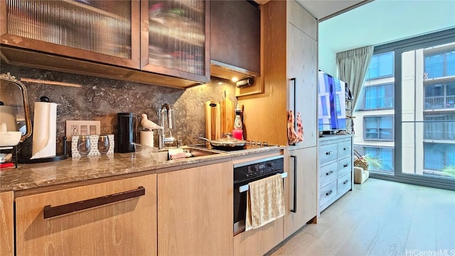 kitchen featuring stone counters, sink, oven, backsplash, and light hardwood / wood-style floors