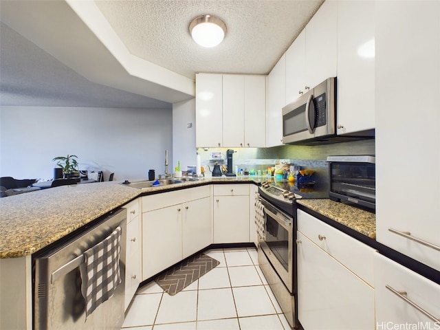 kitchen with a textured ceiling, light tile patterned floors, appliances with stainless steel finishes, kitchen peninsula, and white cabinets