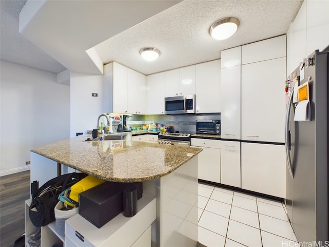 kitchen with stainless steel appliances, white cabinetry, sink, and a textured ceiling