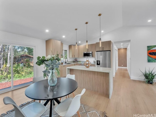 kitchen featuring vaulted ceiling, sink, hanging light fixtures, stainless steel appliances, and light hardwood / wood-style flooring