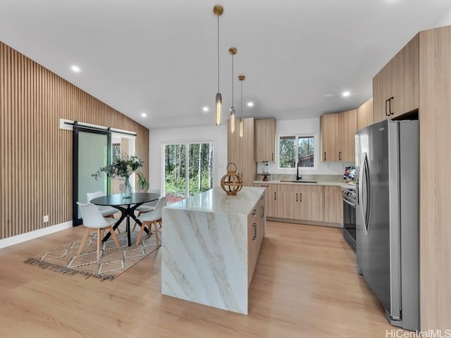 kitchen featuring appliances with stainless steel finishes, light stone counters, a kitchen island, light brown cabinetry, and decorative light fixtures