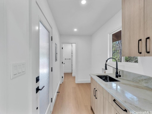 kitchen with sink, light brown cabinets, light stone counters, and light wood-type flooring