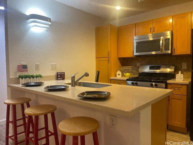 kitchen with sink, light hardwood / wood-style flooring, stainless steel appliances, a kitchen breakfast bar, and tasteful backsplash