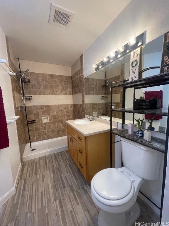 bathroom with a tile shower, hardwood / wood-style floors, vanity, and toilet