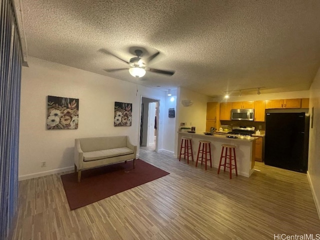 living room with a textured ceiling, ceiling fan, and light wood-type flooring