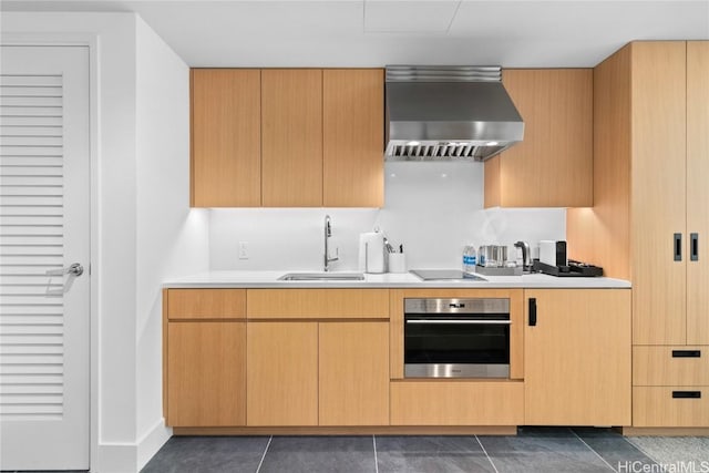 kitchen featuring oven, dark tile patterned floors, a sink, light countertops, and wall chimney range hood