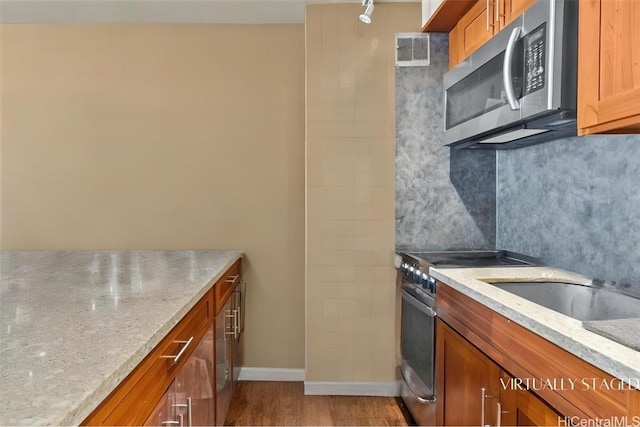 kitchen featuring decorative backsplash, light hardwood / wood-style flooring, light stone countertops, and appliances with stainless steel finishes