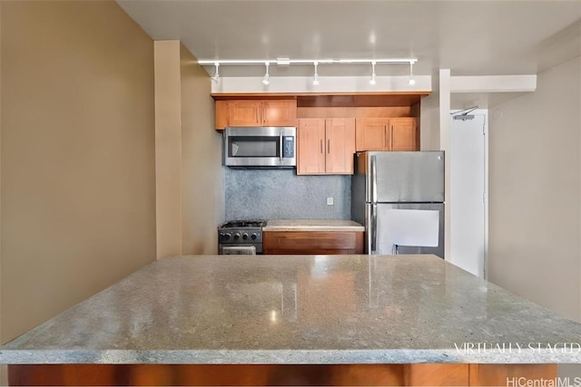 kitchen with stainless steel appliances, rail lighting, light stone countertops, and backsplash