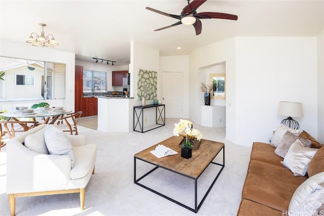 living area featuring light carpet, rail lighting, and ceiling fan with notable chandelier