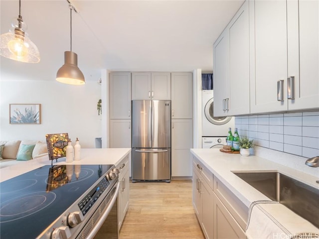 kitchen with stacked washer and clothes dryer, sink, hanging light fixtures, appliances with stainless steel finishes, and light hardwood / wood-style floors