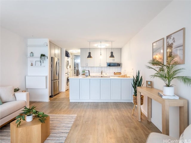 kitchen featuring stainless steel fridge, light hardwood / wood-style flooring, hanging light fixtures, tasteful backsplash, and kitchen peninsula