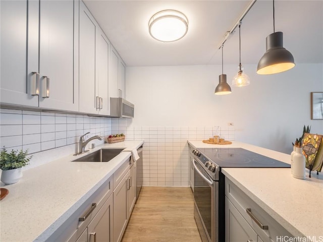 kitchen featuring sink, light wood-type flooring, appliances with stainless steel finishes, pendant lighting, and light stone countertops