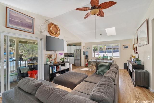 living area with light wood-type flooring, lofted ceiling with skylight, ceiling fan, and baseboards