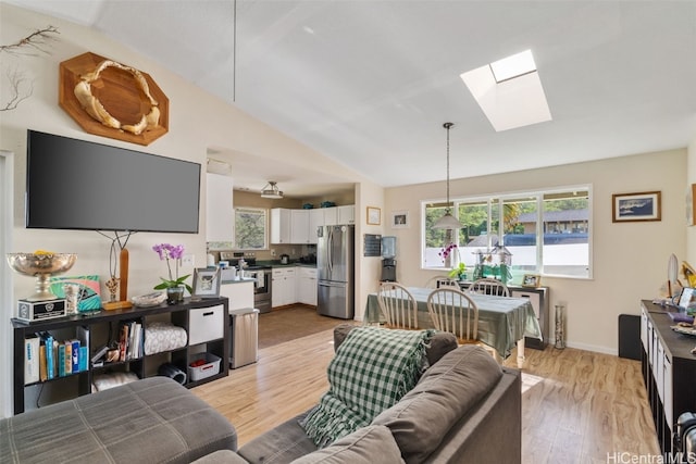 living room with light wood-type flooring, vaulted ceiling with skylight, and baseboards