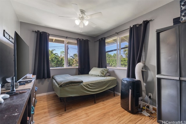 bedroom featuring baseboards, ceiling fan, multiple windows, and light wood-style floors