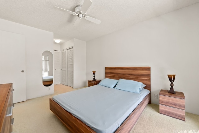 bedroom featuring light carpet, ceiling fan, a closet, and a textured ceiling